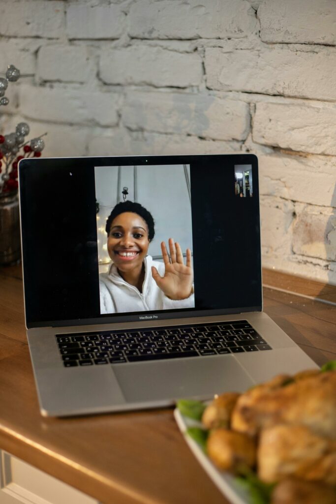 Smiling woman waving during a telehealth video call on a laptop, representing virtual psychiatric care and online mental health appointments available in Maryland.