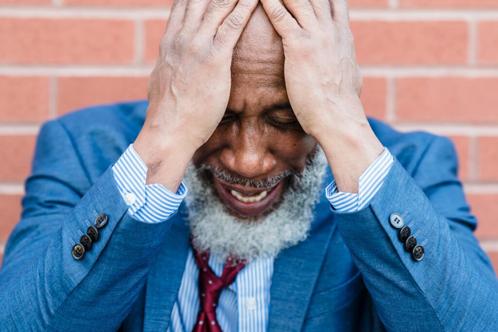 Close-up of a stressed African American man with a beard holding his head, expressing anxiety.