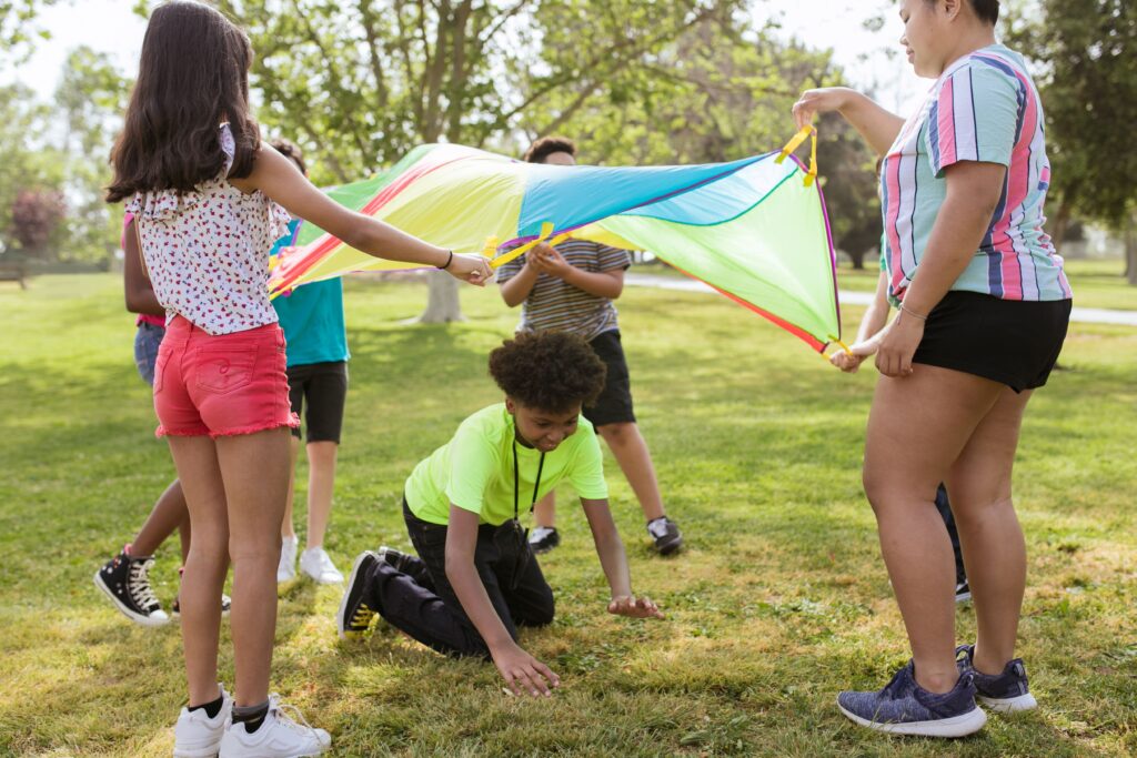 Children playing a parachute game at summer camp while building confidence, friendships, and social skills outdoors.